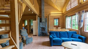 Ein Blockhaus-Interieur mit Kamin aus Stein, einer Holztreppe und einer gemütlichen Sitzecke mit blauem Sofa und Sesseln.
