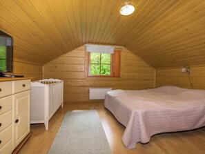 A cozy attic bedroom with a sloped ceiling, a single bed, a dresser, a radiator, and a window with a view of greenery.