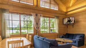 Ein gemütliches Blockhaus-Interieur mit einem Holzesstisch, blauen Sofas und einem an der Wand befestigten Fernseher.