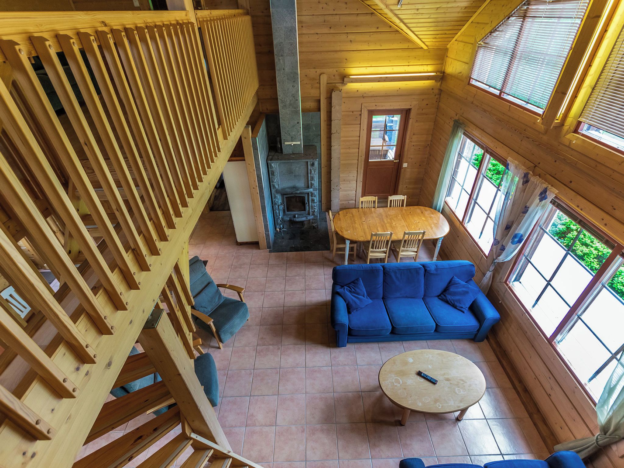 L’intérieur d’un chalet en bois, avec une cheminée en pierre, un canapé bleu, une table à manger et un escalier en bois.