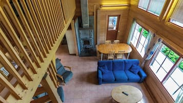 L’intérieur d’un chalet en bois, avec une cheminée en pierre, un canapé bleu, une table à manger et un escalier en bois.