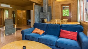 Ein Holzblockhaus-Interieur mit einem blauen Sofa, einem Kamin, Holzmöbeln und einem Balkon.