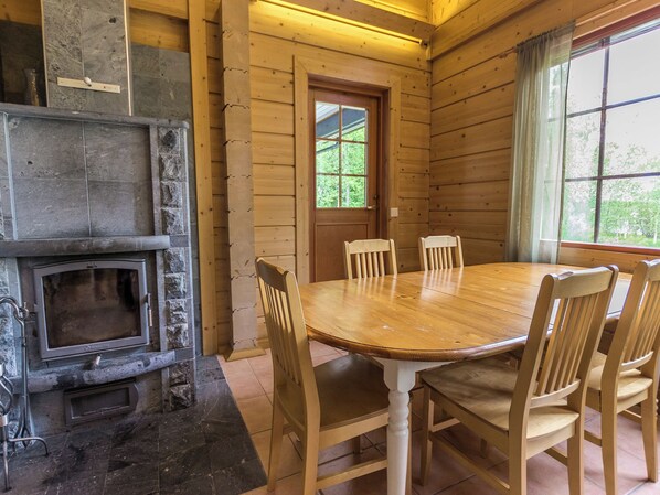 A wooden interior with a stone fireplace, a dining table with chairs, and a window with curtains.