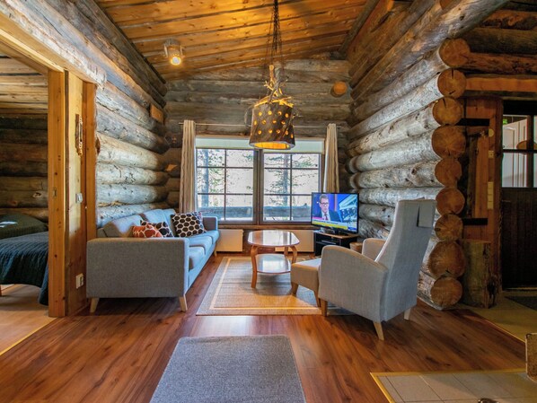 A log cabin interior with a sofa, chairs, a television, and a hanging light fixture.