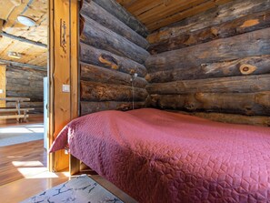 A log cabin room with a bed, wooden walls, and a bench.
