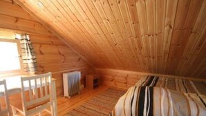 A cozy attic room with wooden walls and a sloped ceiling. There is a bed with a striped bedspread, a chair, and a radiator. - Rantatupa by Interhome (Ruovesi)
