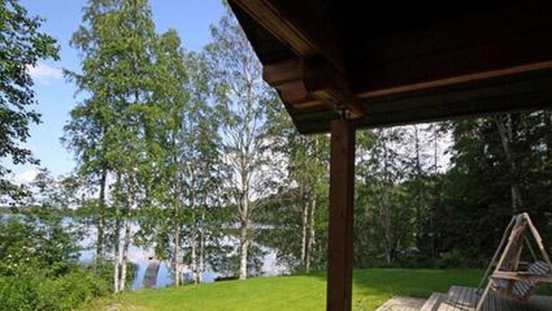 A wooden deck with a swing, surrounded by a grassy area and trees, overlooking a body of water. - Rantatupa by Interhome (Ruovesi)