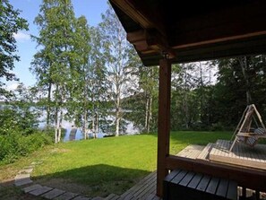 A wooden deck with a swing, surrounded by a grassy area and trees, overlooking a body of water. - Rantatupa by Interhome (Ruovesi)