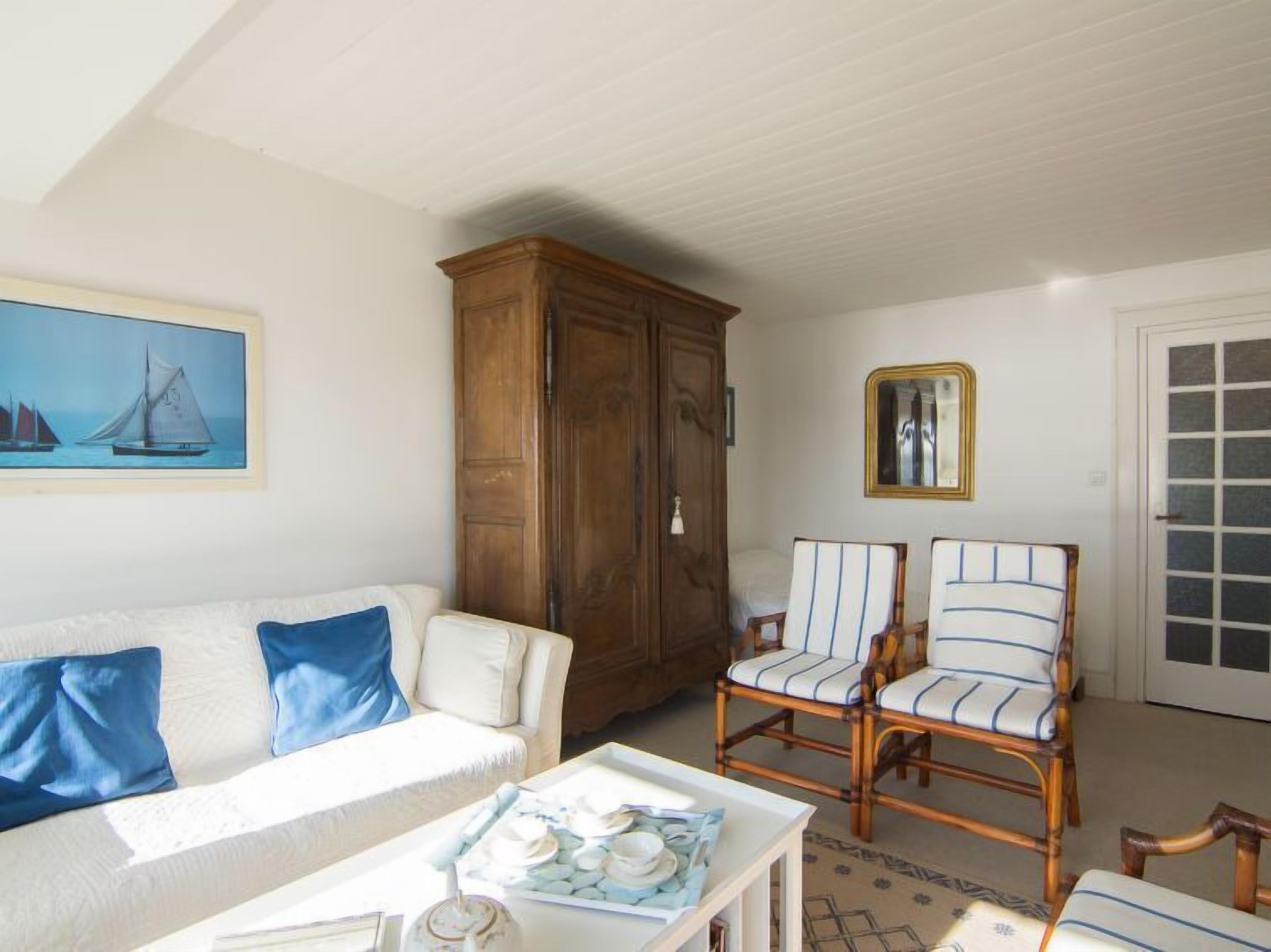 A living room with a white sofa, two striped armchairs, a wooden cabinet, and a painting of sailboats.