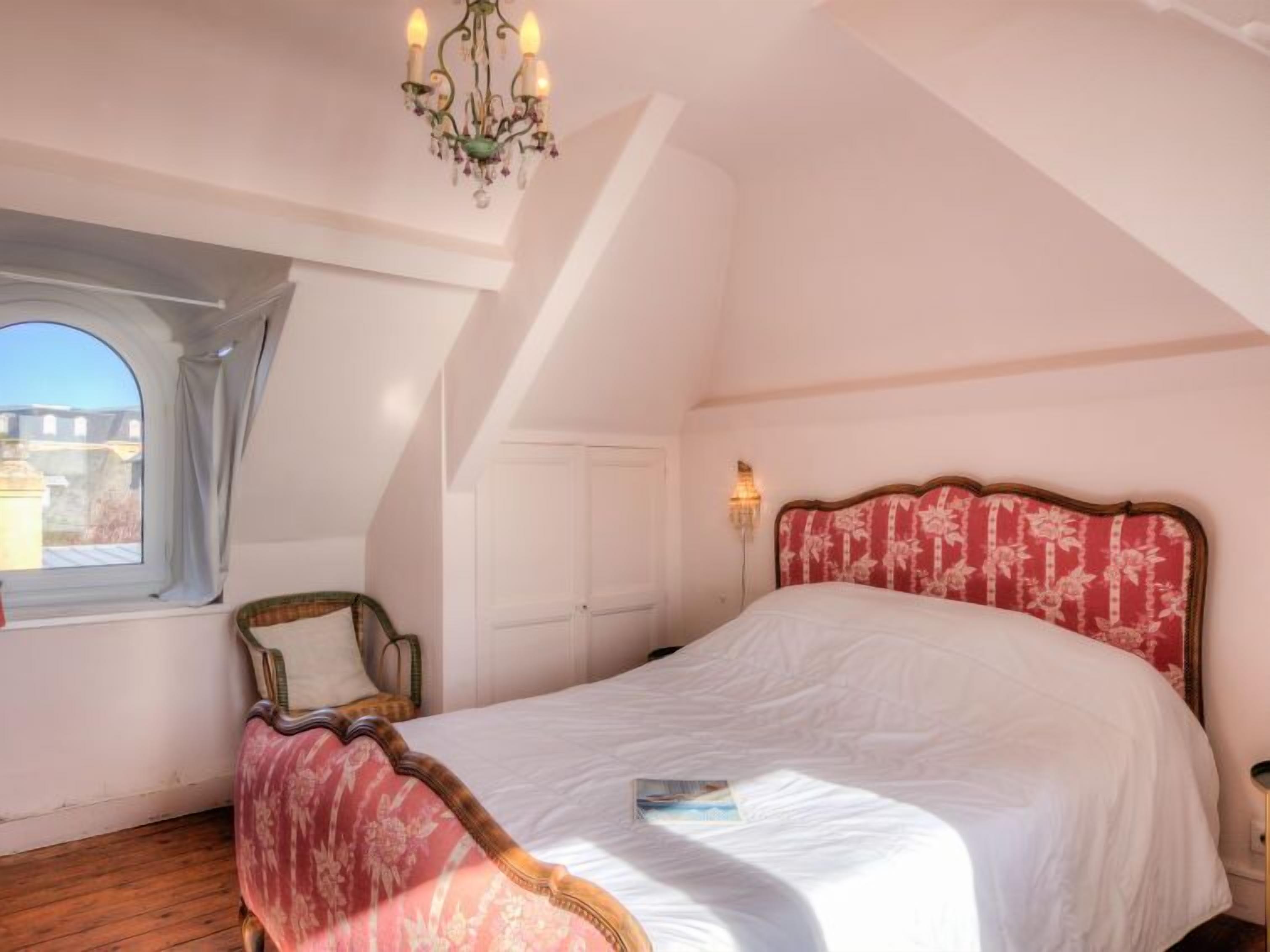 A bedroom with a large bed, a window with a view, a chandelier, and a door.
