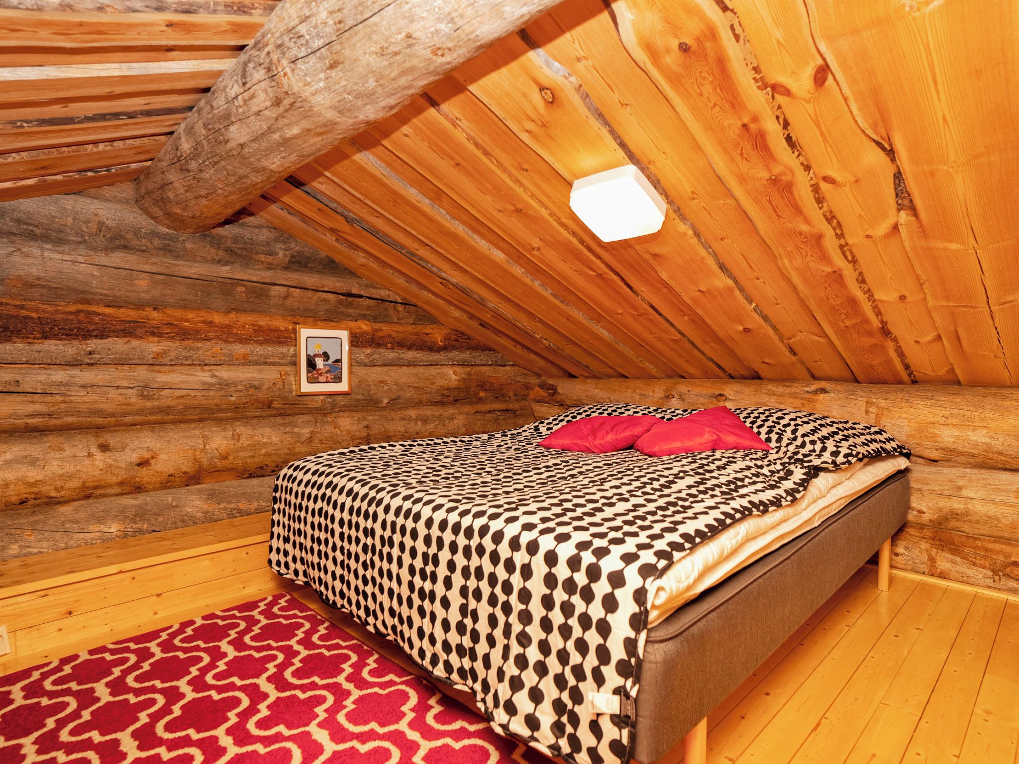 A log cabin bedroom with a bed, a red patterned rug, and a framed picture on the wall.