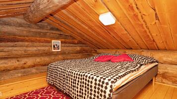A log cabin bedroom with a bed, a red patterned rug, and a framed picture on the wall.
