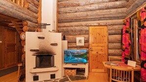 Ein gemütliches Blockhaus-Interieur mit Kamin, Holzwänden, einem Fernseher und einem Essbereich.