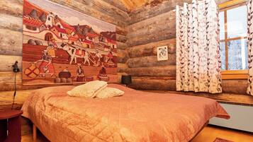 A log cabin bedroom with a large bed, a wooden wall with a mural, a window with curtains, and a small bedside table.