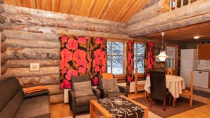 Ein gemütliches Blockhaus-Interieur mit einer Couch, Sesseln, einem Esstisch und einem Kamin.