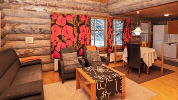 A log cabin interior with a sofa, armchairs, a coffee table, and a dining area.