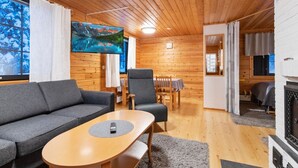 A cozy cabin interior with a wooden ceiling, a sofa, a dining table with chairs, and a fireplace. - Kaltiotievantie 2 mökki 2 by Interhome (Ylläsjärvi)