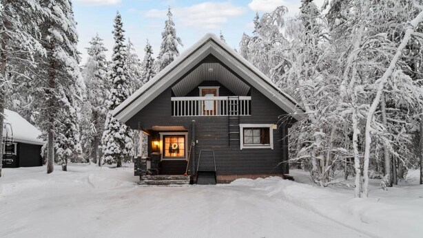 A two-story cabin with a dark exterior, a front porch, and a visible chimney. - Kaltiotievantie 2 mökki 2 by Interhome (Ylläsjärvi)