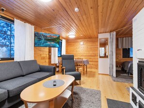 A cozy cabin interior with a sofa, armchair, dining table, and a fireplace. - Kaltiotievantie 2 mökki 2 by Interhome (Ylläsjärvi)