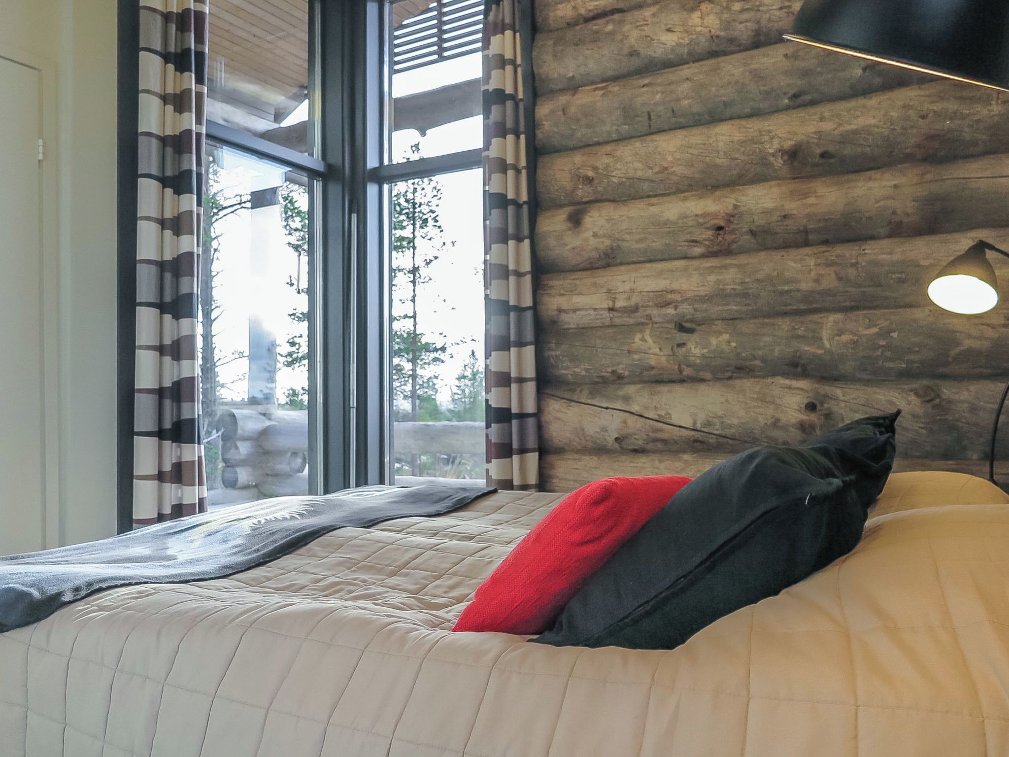 Une chambre avec une grande fenêtre, un lit recouvert d’une courtepointe et un mur fait de rondins de bois.