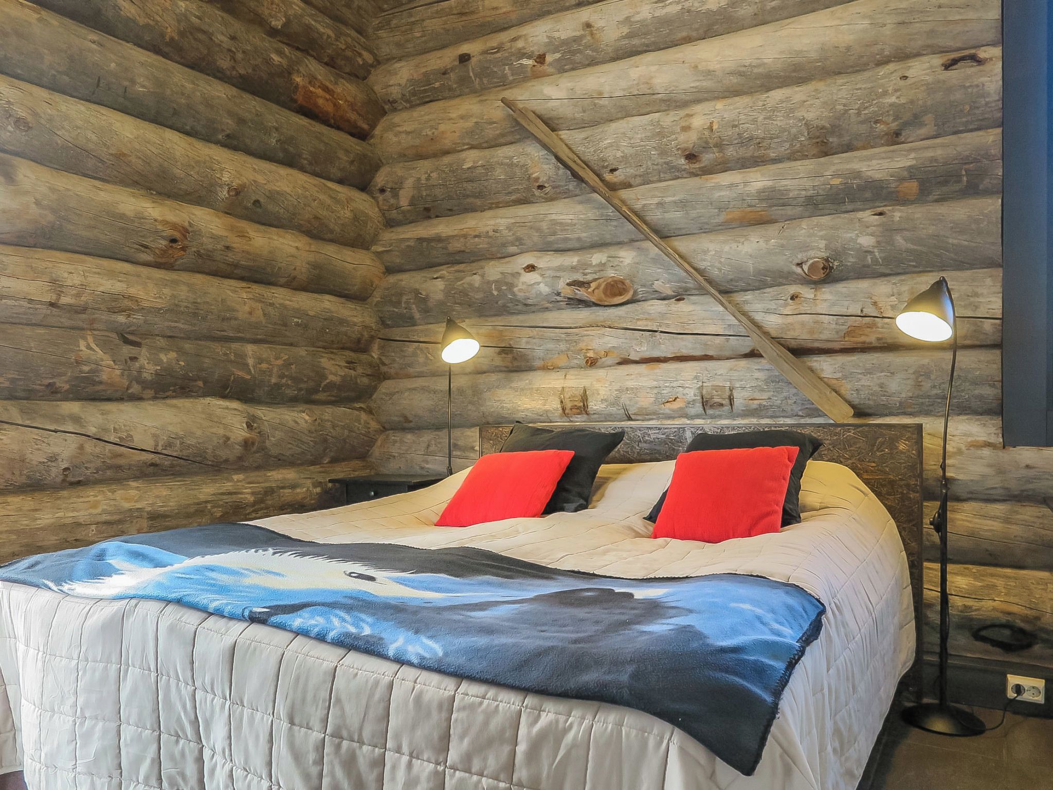 A log cabin bedroom with a bed, two bedside lamps, and a view of the outside.