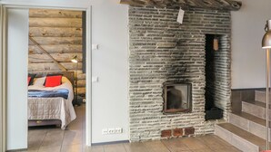 Een kamer met een stenen openhaard, een bed met rode en zwarte kussens, en een trap naar een hoger gelegen verdieping.