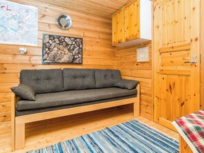Interno di una baita di legno con un divano, una mappa appesa al muro e una porta.