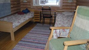 Une chambre confortable dans un chalet, avec deux lits simples, un bureau en bois, une chaise et une vue sur un paysage enneigé par la fenêtre.