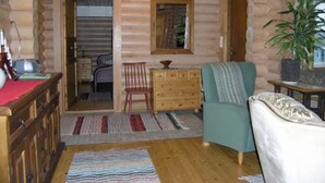 L’intérieur d’un chalet accueillant, avec un plancher en bois, un fauteuil vert, une commode en bois et une petite table sur laquelle est posée une plante.