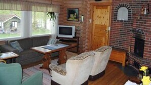 Un intérieur de chalet chaleureux avec une cheminée, des murs en bois, un téléviseur et un coin salon confortable.