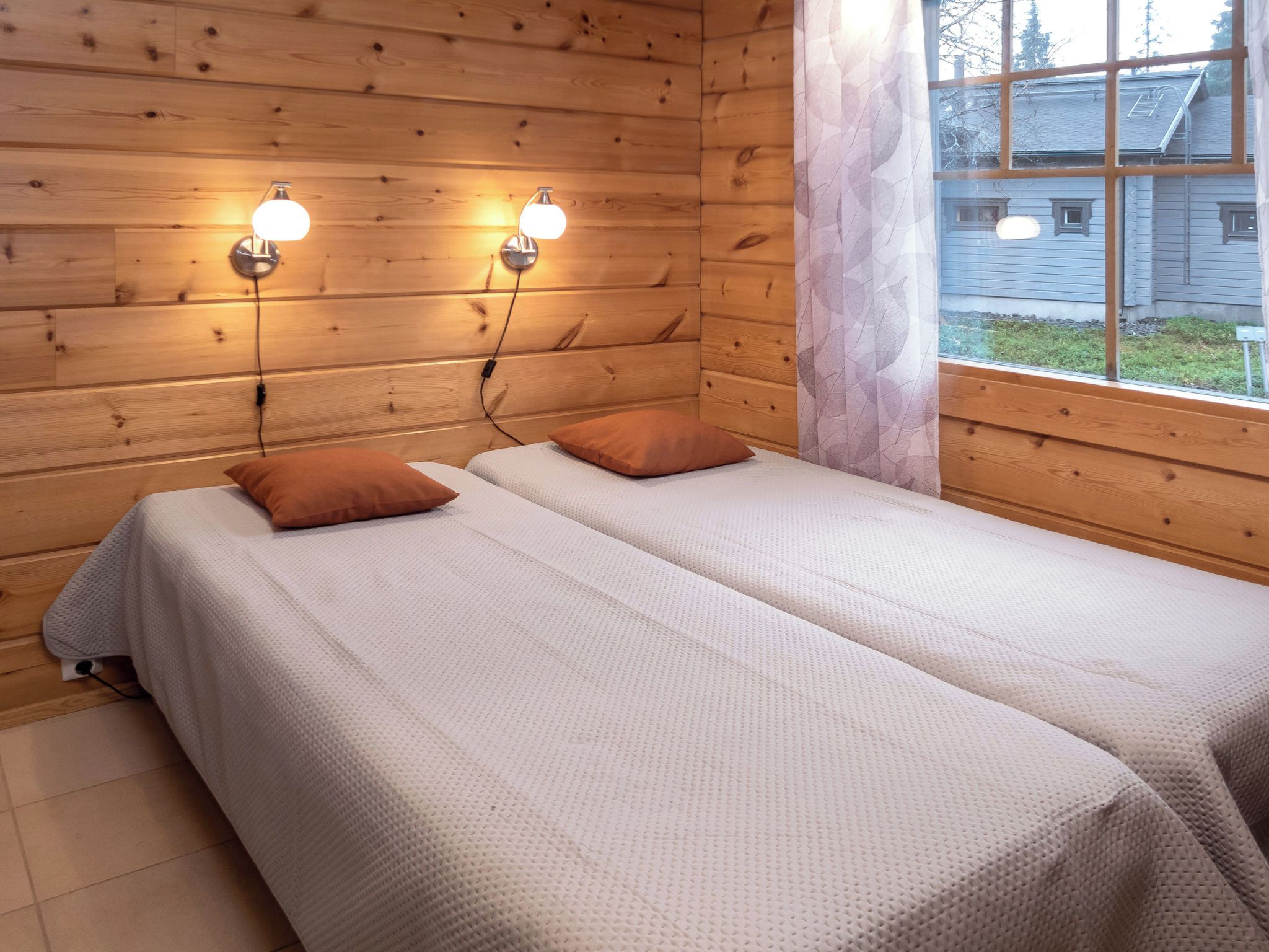 A wooden cabin room with two beds, a window, and wall-mounted lights.