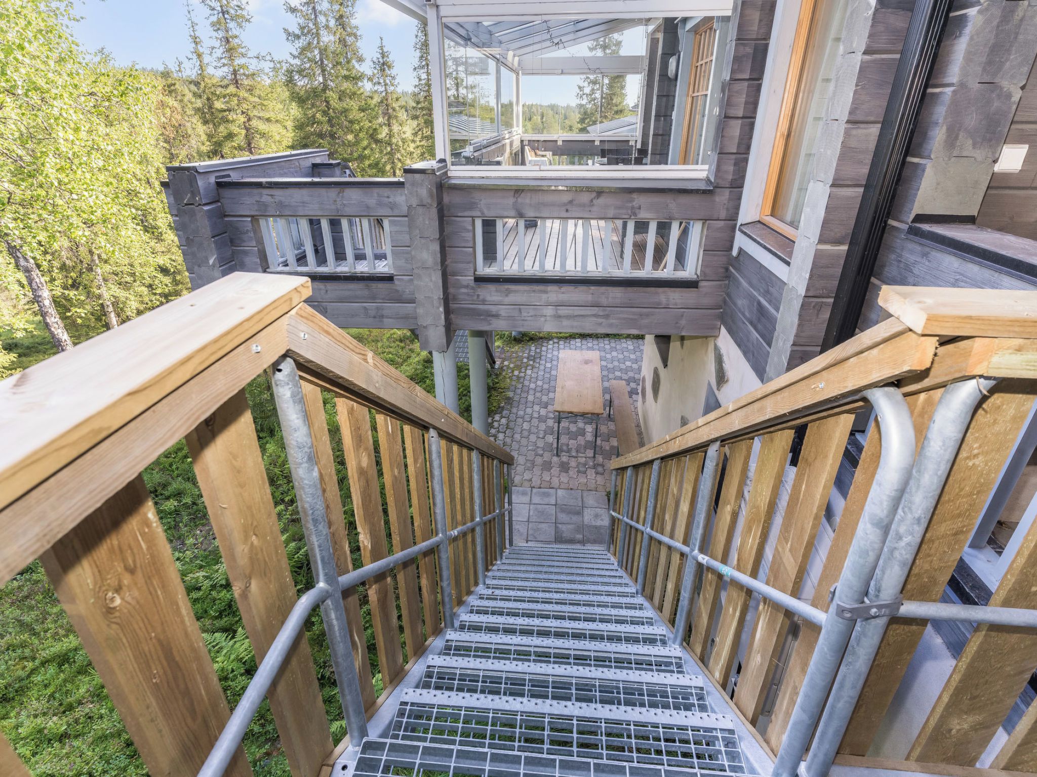 Un escalier en bois mène à un bâtiment doté de nombreuses fenêtres et offrant une vue sur les arbres.