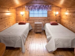 Une chambre confortable dans un chalet, avec deux lits, une petite commode et une fenêtre avec des stores.