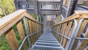 A wooden staircase leading to a glass-enclosed upper level with a view of the surrounding forest.
