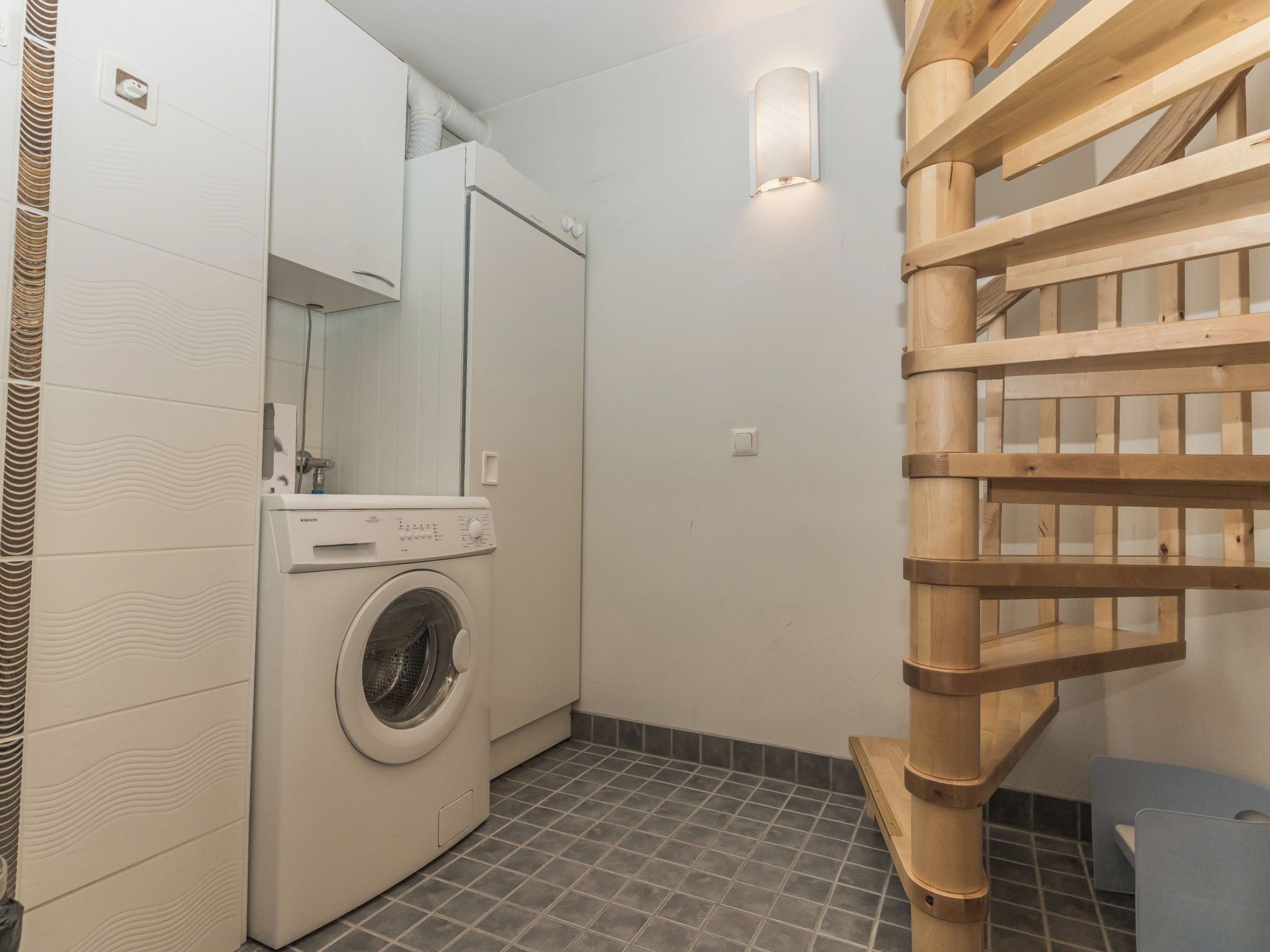 Ein kleiner Hauswirtschaftsraum mit Waschmaschine, Trockner und einer Holztreppe.