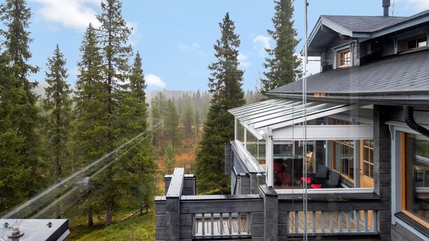 A modern house with a large deck, surrounded by a forest.