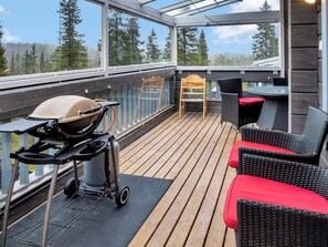En overdækket terrasse med grill, fletmøbler og udsigt til træer.