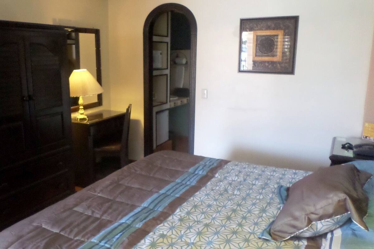 Ein Schlafzimmer mit einem Bett, einem Schreibtisch, einem Stuhl, einem Kleiderschrank und einer Lampe.