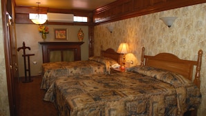 A bedroom with two beds, a wooden headboard, a nightstand with a lamp, a vase with flowers, and a fireplace. - El Dorado Inn (Delicias)