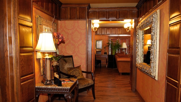A hallway with wooden paneling, a table with a lamp, a chair, and a mirror. - El Dorado Inn (Delicias)