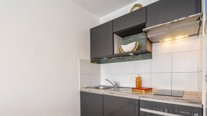 A compact kitchen with dark cabinets, a white backsplash, and a wooden chair. - Le Forum by Interhome (Royan)