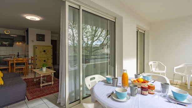 A dining area with a table set for two, a sofa, and a kitchen in the background. - Le Forum by Interhome (Royan)