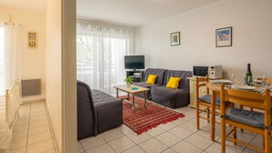 A modern living room with a sofa, TV, dining table, and chairs. - Le Forum by Interhome (Royan)