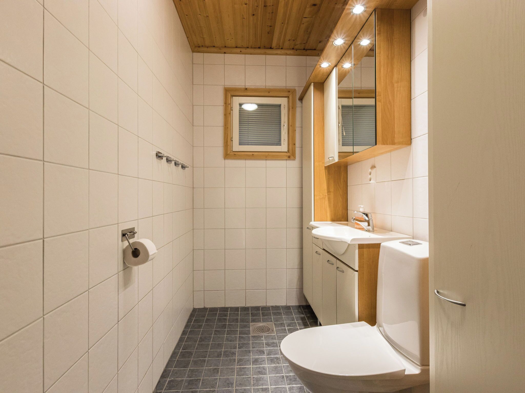 Een kleine badkamer met toilet, wastafel en een raam.