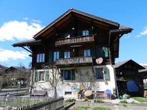 Un chalet traditionnel en bois, doté d’un balcon, d’un petit jardin et surplombant un ciel d’un bleu éclatant.