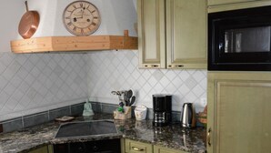 Une cuisine avec des meubles de couleur verte, une cuisinière noire, une machine à café et une horloge au mur.