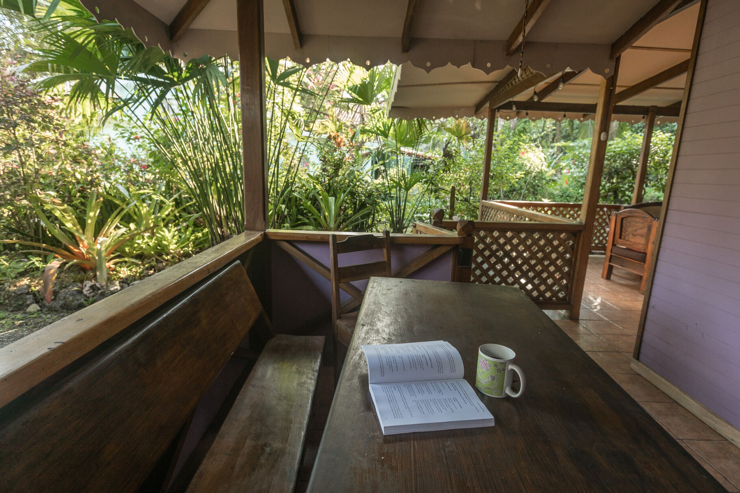 Een houten bank met een boek en een mok, onder een houten pergola met uitzicht op groen.
