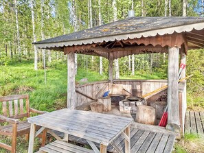 A wooden outdoor structure with a bench and a table, surrounded by a forest. - Honkakoti by Interhome (Kuopio)