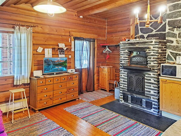 A cozy cabin interior with wooden walls, a stone fireplace, a wooden dresser, and a television.