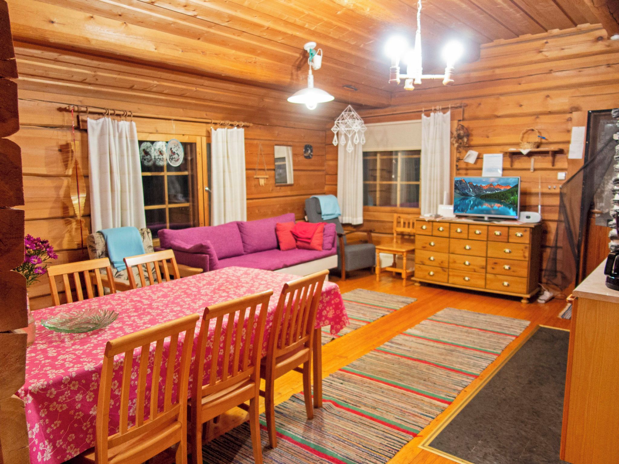 A cozy cabin interior with a dining area, a sofa, a TV, and a wooden dresser.